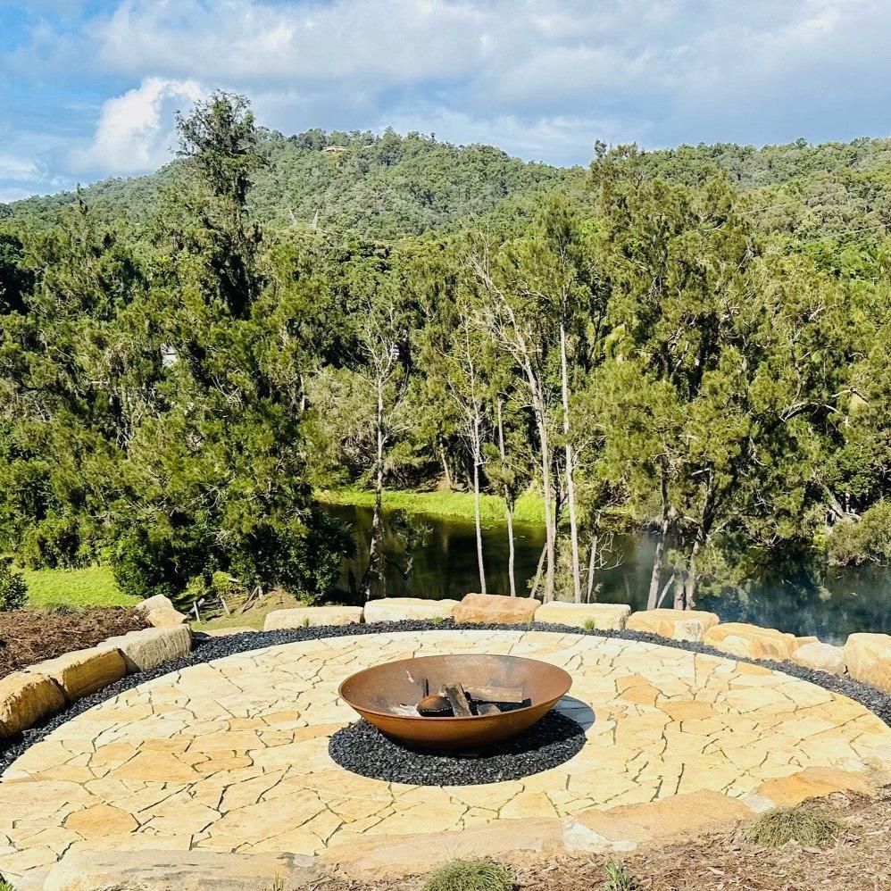 The Crucible Fire Pit sitting on gravel rocks in a designated firepit area overlooking a creek