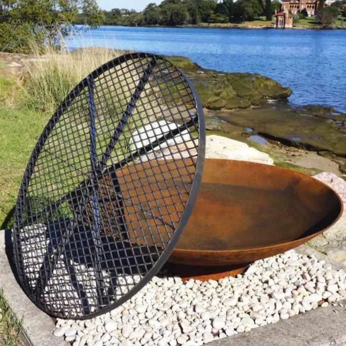 BBQ Fire Pit Metal Cooking Grill leaning against a fire pit near a lake