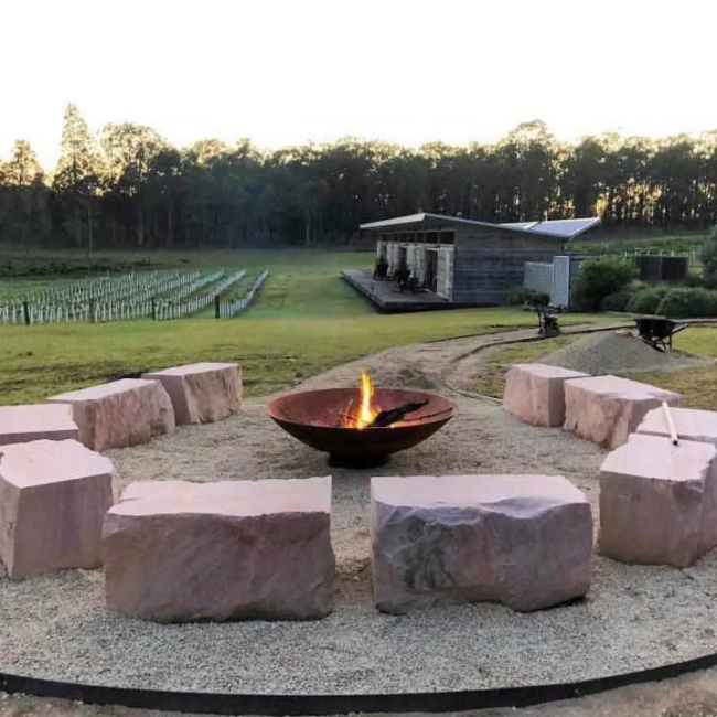 The Cauldron Fire Pit 1500mm in rural setting with large stone seats around it