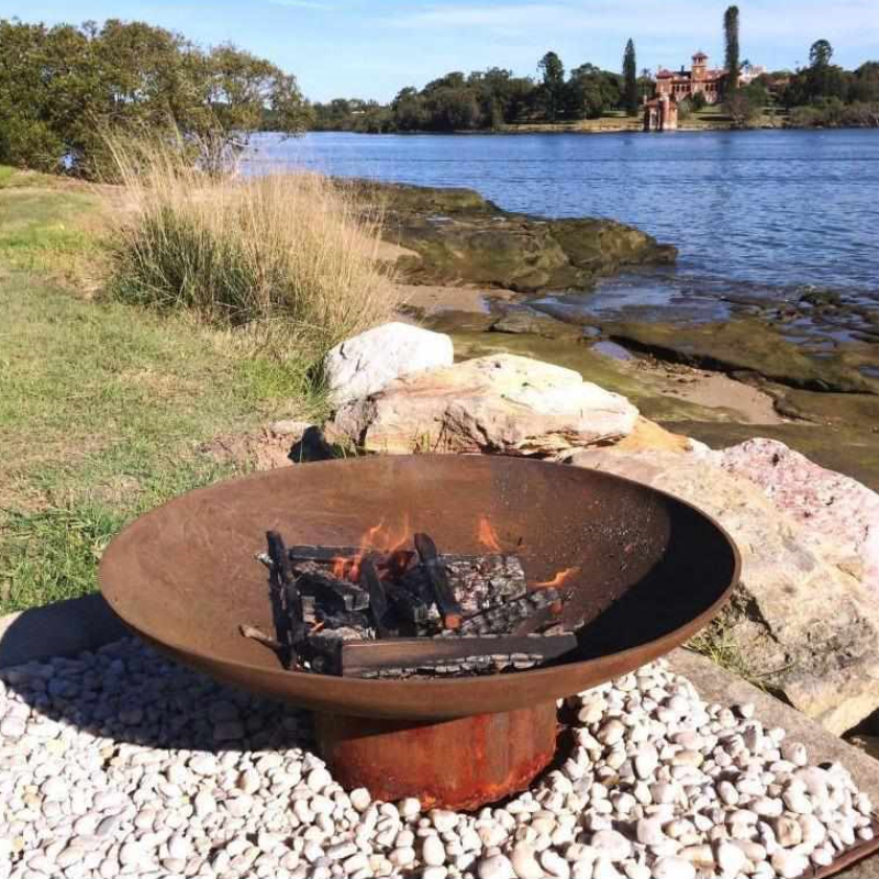 The Cauldron Cast Iron Fire Pit in rust with a small fire burning