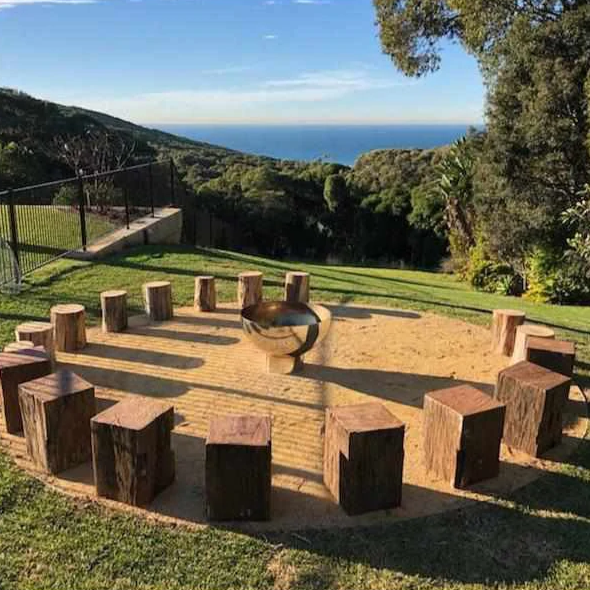 The Goblet Stainless Steel Fire Pit in the middle of log seats